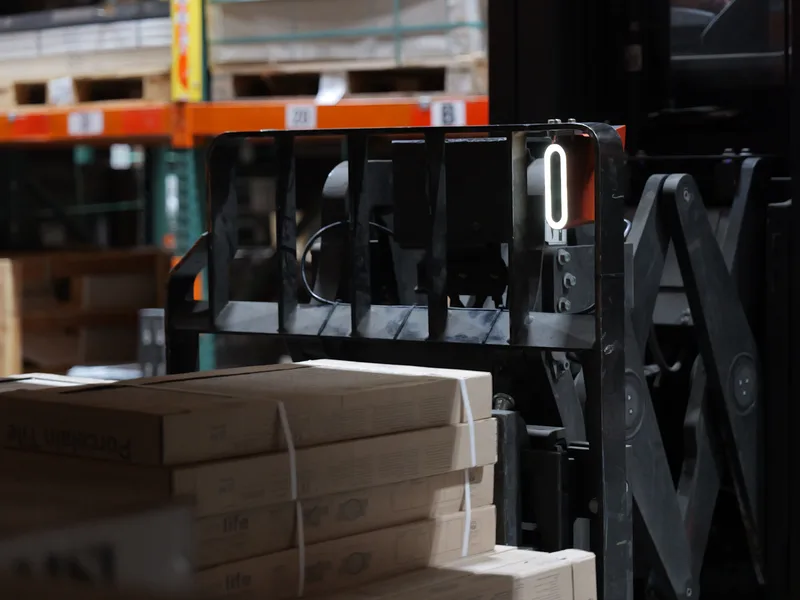 Corvus Trident AI copilot device mounted to a reach truck gate in a distribution center, with pallets in the foreground