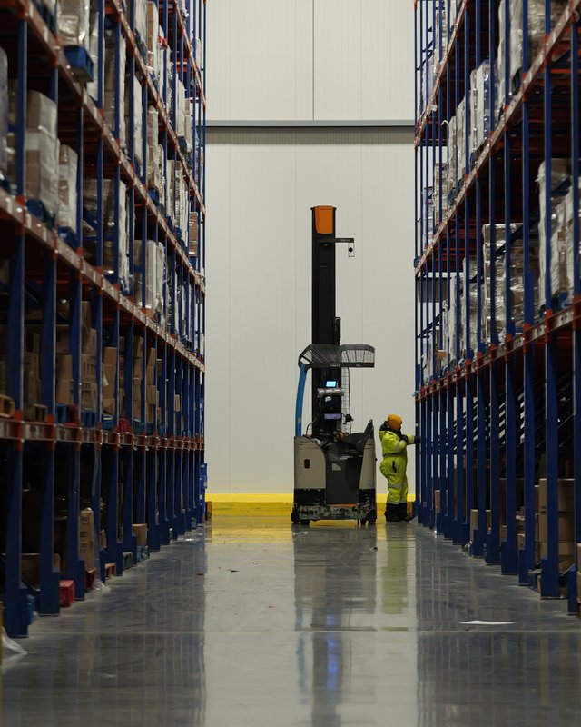Worker operating a reach truck in a cold storage warehouse aisle