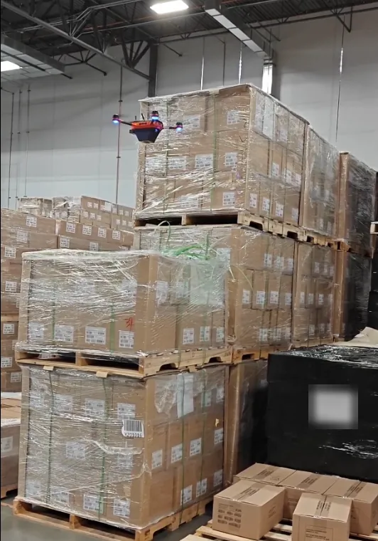 Corvus One autonomous warehouse inventory drone flying beside floor-stacked, shrink-wrapped pallets in a bulk storage area with no racking