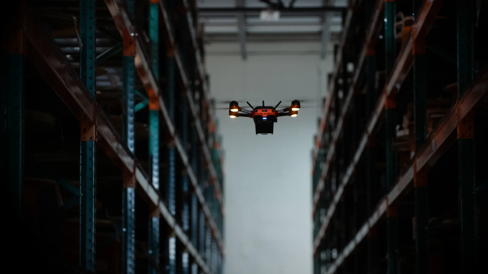 Corvus One autonomous inventory drone flying down an aisle between tall pallet racks in a distribution center