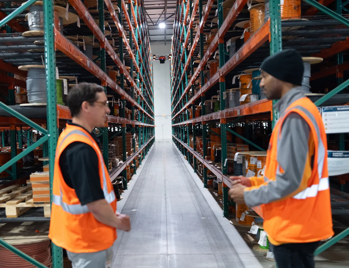 Two warehouse operations managers watch a Corvus One autonomous drone scan inventory in a large distribution center aisle