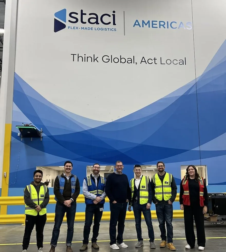 Members of the Staci Americas and Corvus Robotics teams standing together in front of a wall-mounted Corvus One landing pad at Staci's distribution center
